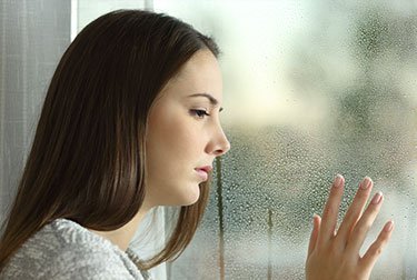 woman looking out through window with one hand resting on glass